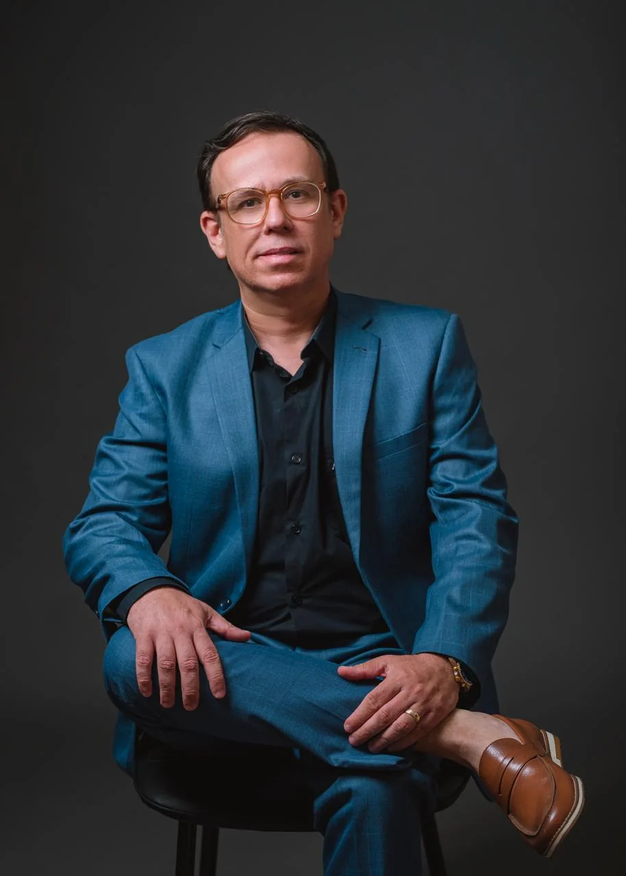 Bruno Benevides em retrato profissional, sentado, com terno azul